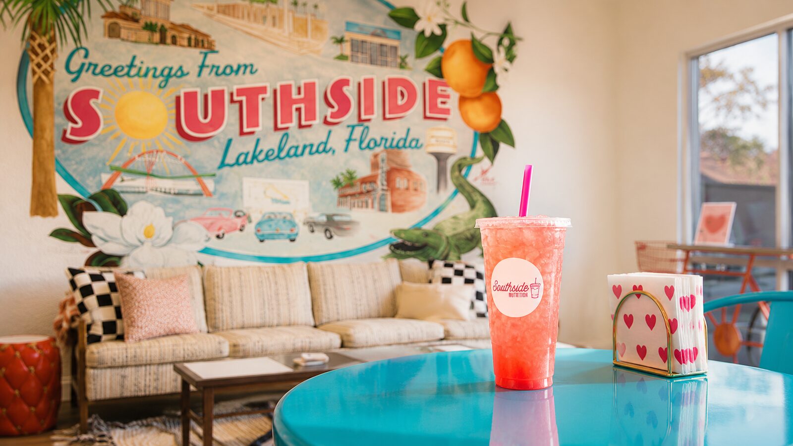 Pink loaded tea on a teal table in front of the Greetings from Southside Lakeland mural